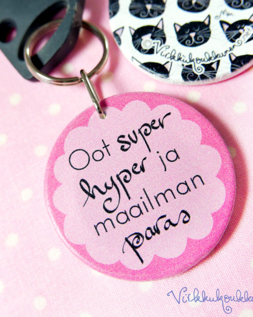 Pyöreä puinen Suomessa valmistettu Virkkukoukkusen suunnittelema vaaleanpunainen avaimenperä "Oot super hyper ja maailman paras" - tekstillä.