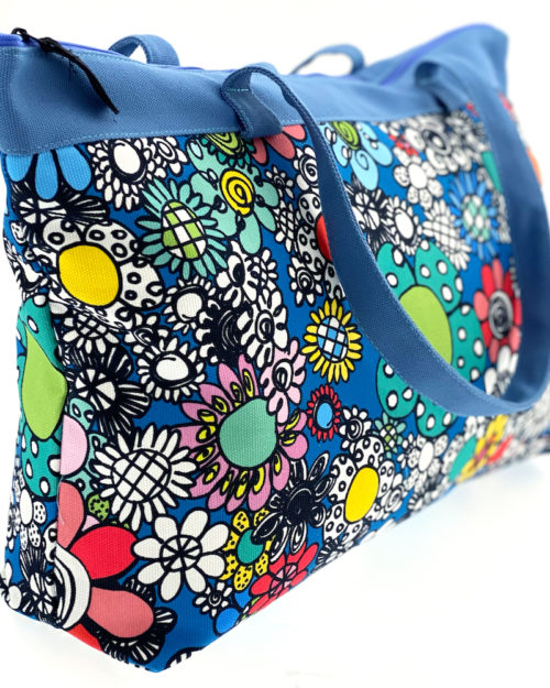 Virkkukoukkusen suunnittelema Suomessa tehty Reilu-laukku vetoketjullisella sisätaskulla. Kuosina kaunis musta-valko-värikäs Kukkaralla sinisellä pohjalla ja sinisillä kantohihnoilla.