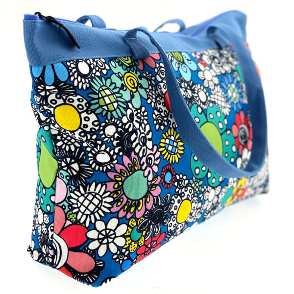 Virkkukoukkusen suunnittelema Suomessa tehty Reilu-laukku vetoketjullisella sisätaskulla. Kuosina kaunis musta-valko-värikäs Kukkaralla sinisellä pohjalla ja sinisillä kantohihnoilla.